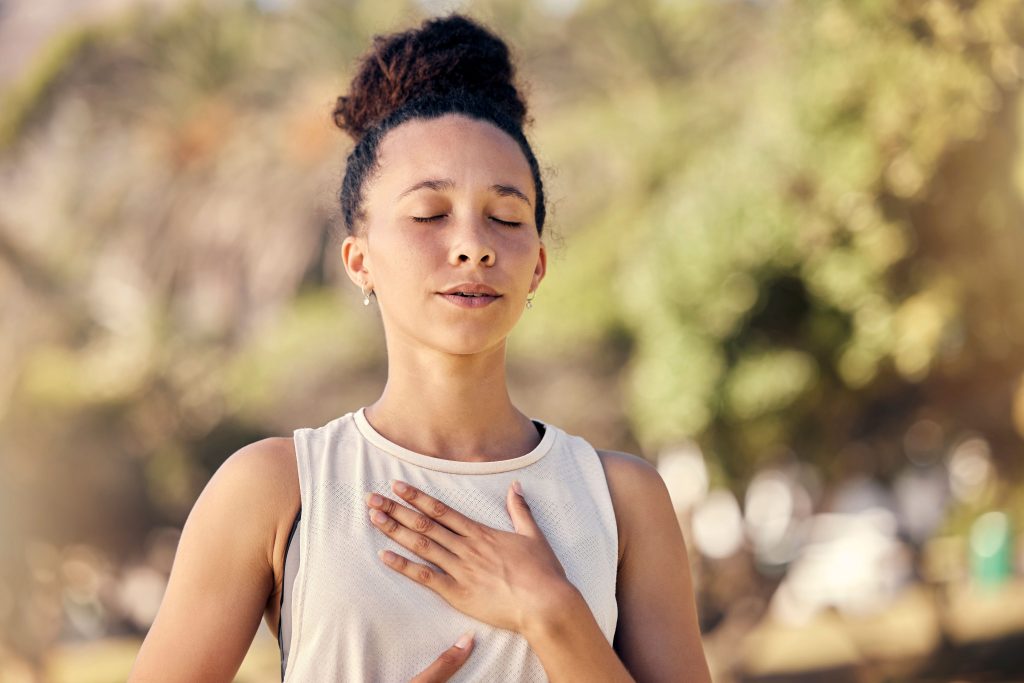 Femme les yeux fermés, une main posée sur le cœur, respirant en extérieur