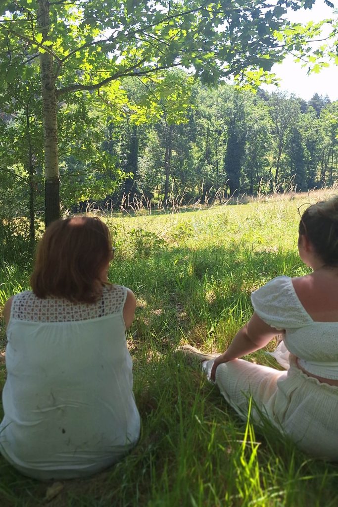 Deux participantes assises de dos dans l'herbe face à une prairie boisée