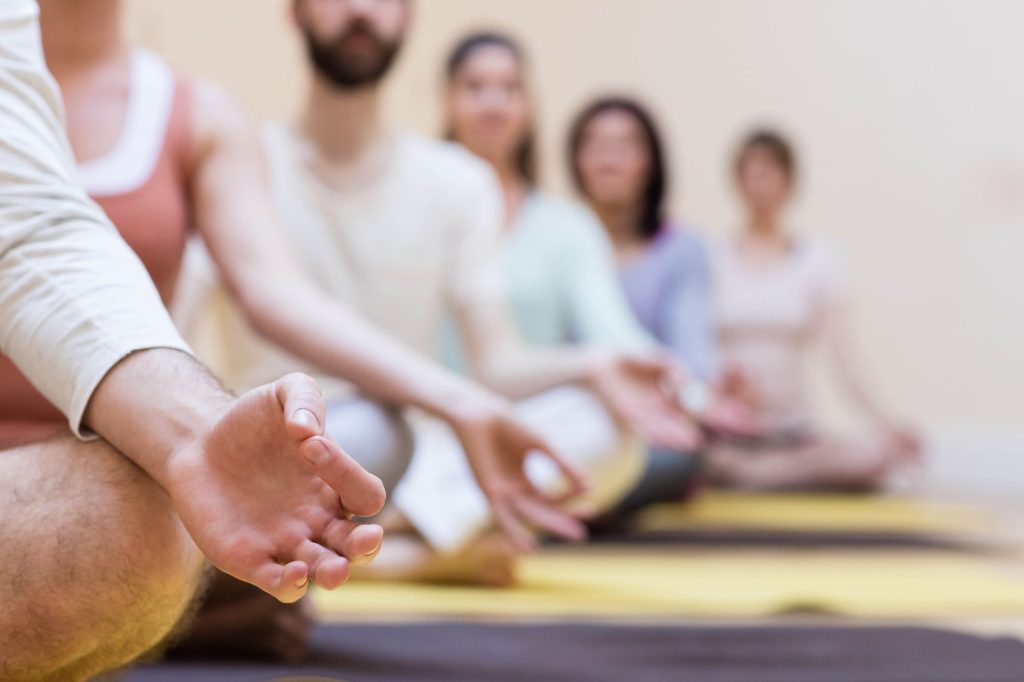 Groupe de personnes assises en tailleur sur des tapis pendant une séance de sophrologie collective